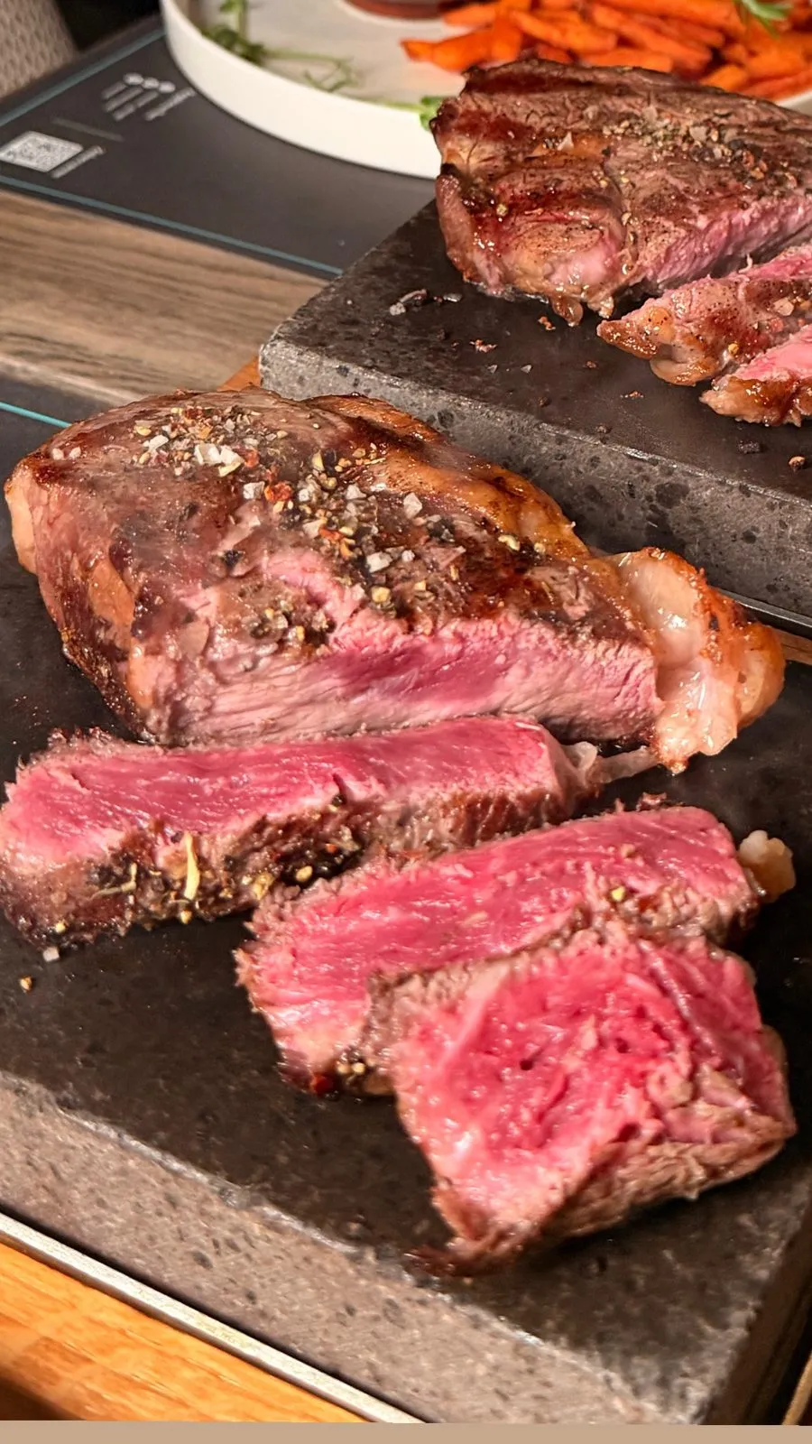 Plastry steku medium rare z różowym miąższem i chrupiącą, przyprawioną skórką na desce.